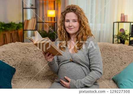 Pregnant woman reading motherhood book at home smiling gently thoughtful and emotional expression Pregnant woman reading motherhood book at home smiling gently thoughtful and emotional expression 129227308