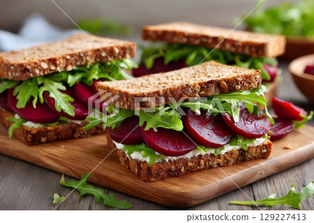 Healthy beetroot sandwiches with goat cheese and arugula on wooden cutting board 129227413