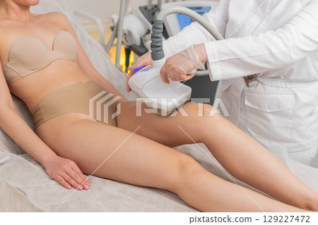 Doctor makes woman cavitation LPG vacuum roller massage on legs, correction figures in spa clinic Doctor makes woman cavitation LPG vacuum roller massage on legs, correction figures in spa clinic 129227472