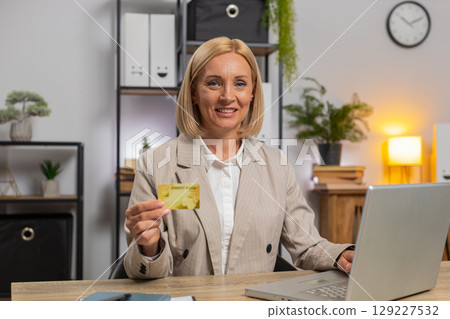 Mature businesswoman using bank credit card and laptop for online shopping payments at home office Mature businesswoman using bank credit card and laptop for online shopping payments at home office 129227532