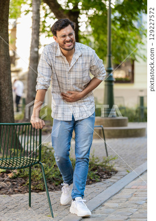 Indian young man traveler feeling sudden strong abdominal stomach ache, gastritis problem on street Indian young man traveler feeling sudden strong abdominal stomach ache, gastritis problem on street 129227572
