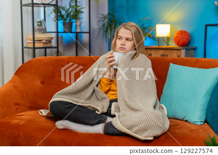 Teenager boy sick with cold and allergy, covered with blanket, drinking warm tea, coughing at home Teenager boy sick with cold and allergy, covered with blanket, drinking warm tea, coughing at home 129227574