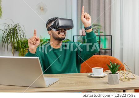 Indian man using virtual reality futuristic technology headset play simulation 3D video game at home 129227582