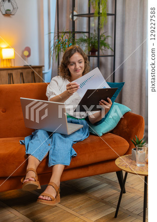 Woman accountant using laptop working with financial graph documents, reports of home income on sofa Woman accountant using laptop working with financial graph documents, reports of home income on sofa 129227588