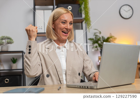 Happy Caucasian businesswoman celebrating success reading great news on laptop at home office desk Happy Caucasian businesswoman celebrating success reading great news on laptop at home office desk 129227590