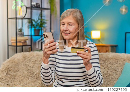 Mature woman shopping online on smartphone entering credit card info satisfied with purchase at home Mature woman shopping online on smartphone entering credit card info satisfied with purchase at home 129227593