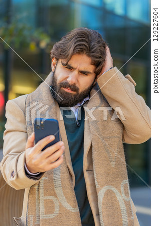 Upset Indian man using smartphone browsing, loses becoming shocked bad news on downtown city street 129227604