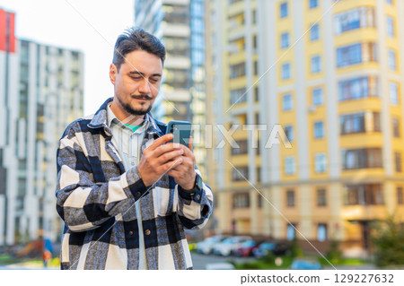 Smiling mature man tourist chatting on internet via mobile phone standing on downtown city street 129227632