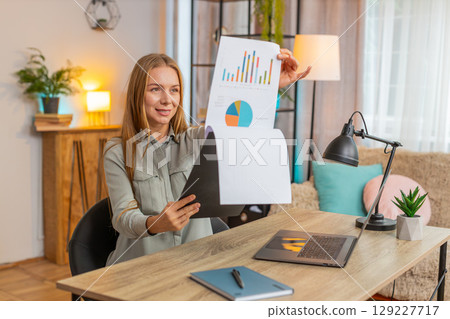 Happy mature businesswoman freelancer analyzing graph documents sitting at home office table desk 129227717