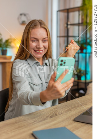 Happy mature woman freelancer using smartphone celebrating success victory winning lottery at table 129227719