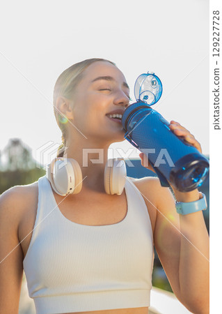Athletic fit sport runner girl woman drinking water from bottle after training exercise in park Athletic fit sport runner girl woman drinking water from bottle after training exercise in park 129227728