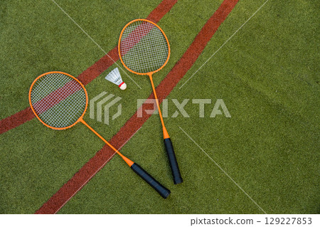 Two orange badminton rackets and a shuttlecock rest on a green sports field, captured from above Two orange badminton rackets and a shuttlecock rest on a green sports field, captured from above 129227853