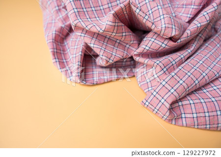 Pink plaid fabric with soft folds on beige background, textile material close-up. 129227972