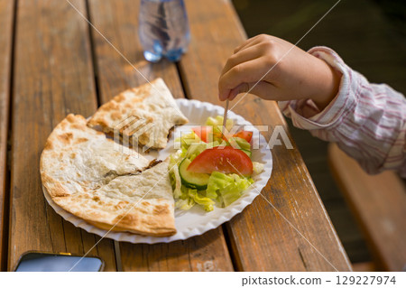 Childs hand picking salad from a plate with quesadilla on a rustic wooden table 129227974