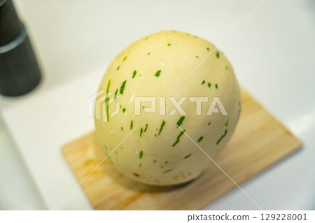 A close-up of a peeled melon with green streaks on a wooden cutting board. 129228001
