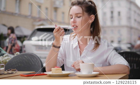 A woman savoring a slice of cake at an outdoor caf with a warm ambience 129228115