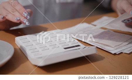 A closeup view of hands skillfully using a calculator, with cash, documents, and files scattered on a wooden table A closeup view of hands skillfully using a calculator, with cash, documents, and files scattered on a wooden table 129228121