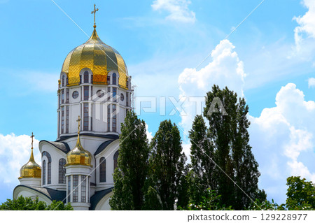 Bright shiny Christian church with golden domes, blue clear sky 129228977