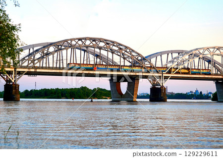 A large railway bridge with passenger train on an evening calm river A large railway bridge with passenger train on an evening calm river 129229611