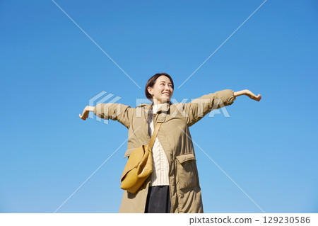 Woman, middle age, spreading arms and taking a deep breath, blue sky 129230586