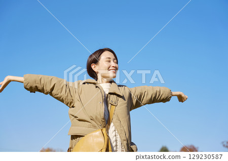 Woman, middle age, spreading arms and taking a deep breath, blue sky 129230587