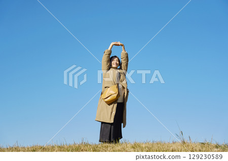 Woman, middle age, stretching, blue sky, whole body Woman, middle age, stretching, blue sky, whole body 129230589