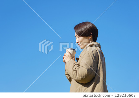 Middle-aged woman drinking coffee, blue sky 129230602