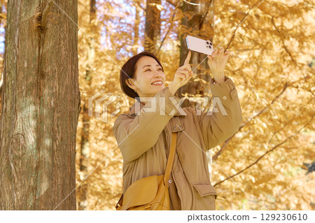 Middle-aged woman taking video of autumn leaves with her smartphone Middle-aged woman taking video of autumn leaves with her smartphone 129230610