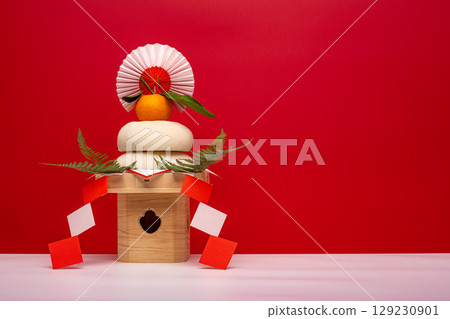 A photo of a real rice cake, "Kagami-mochi," placed on the left, on a red and white background, with a sanpo (pedestal) A photo of a real rice cake, "Kagami-mochi," placed on the left, on a red and white background, with a sanpo (pedestal) 129230901
