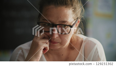 Exhausted Female Teacher Taking Off Glasses, Sitting Alone in Empty Classroom, Feeling Stress 129231302