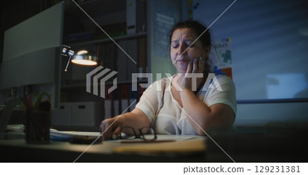Exhausted Female Teacher Sitting at Computer in Empty Classroom Late at Night Exhausted Female Teacher Sitting at Computer in Empty Classroom Late at Night 129231381