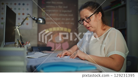Female Teacher Sitting at Desk, Checking Homework of Students, Grading School Tests After Class 129231395