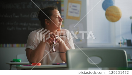 Tired Female Teacher Sitting Alone at the Desk in Empty Classroom, Relaxing After Class Tired Female Teacher Sitting Alone at the Desk in Empty Classroom, Relaxing After Class 129231452
