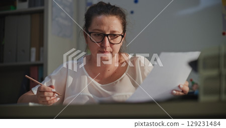 Female Teacher Grading Writing Tasks or Homework, Checking School Exam, Sitting at Desk 129231484