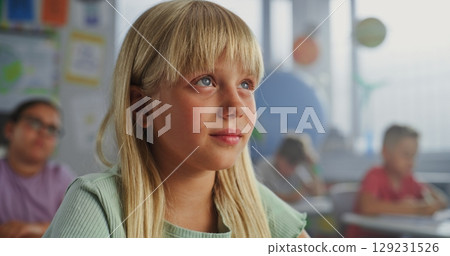 Close Up of Elementary School Girl Sitting at Desk, Raising Hand and Answering Teacher's Question Close Up of Elementary School Girl Sitting at Desk, Raising Hand and Answering Teacher's Question 129231526