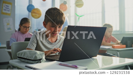 Computer Science Lesson: Primary School Boy Sitting at Desk, Using Laptop in Classroom 129231538
