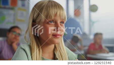 Close Up of Elementary School Girl Sitting at Desk, Raising Hand and Answering Teacher's Question 129231540