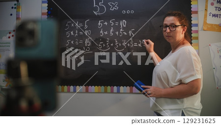 Female Teacher Writing on Chalkboard, Explaining Math During Video Call or Recording Lesson Female Teacher Writing on Chalkboard, Explaining Math During Video Call or Recording Lesson 129231625