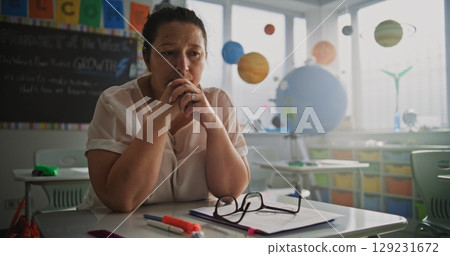 Tired Female Teacher Sitting Alone at the Desk in Empty Classroom, Feeling Burnout and Mental Exhaustion 129231672