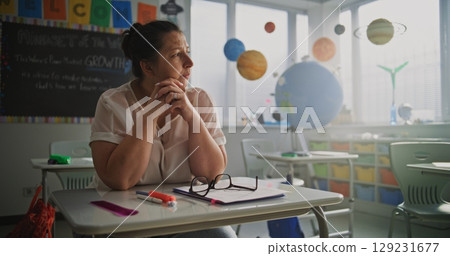 Tired Female Teacher Sitting Alone at the Desk in Empty Classroom, Feeling Burnout and Mental Exhaustion 129231677