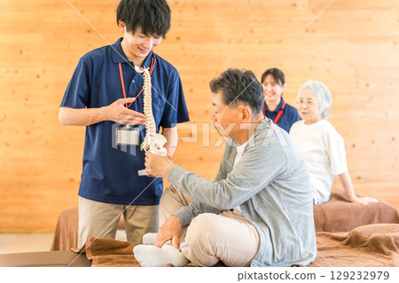 一名男性物理治療師（復健、運動矯形、訓練師）正在用骨骼標本向一位老年男性講解 129232979