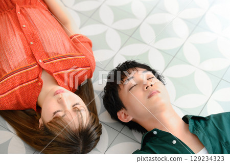 A man and a woman lying side by side on the floor with their eyes closed A man and a woman lying side by side on the floor with their eyes closed 129234323