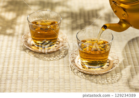Pouring barley tea from a kettle into a glass on a tatami mat gives you a cool, Japanese summer feeling. Pouring barley tea from a kettle into a glass on a tatami mat gives you a cool, Japanese summer feeling. 129234389