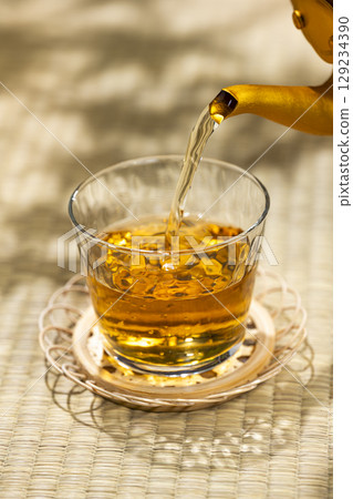 Pouring barley tea from a kettle into a glass on a tatami mat gives you a cool, Japanese summer feeling. Pouring barley tea from a kettle into a glass on a tatami mat gives you a cool, Japanese summer feeling. 129234390
