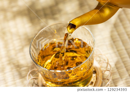 Pouring barley tea from a kettle into a glass on a tatami mat gives you a cool, Japanese summer feeling. Pouring barley tea from a kettle into a glass on a tatami mat gives you a cool, Japanese summer feeling. 129234393