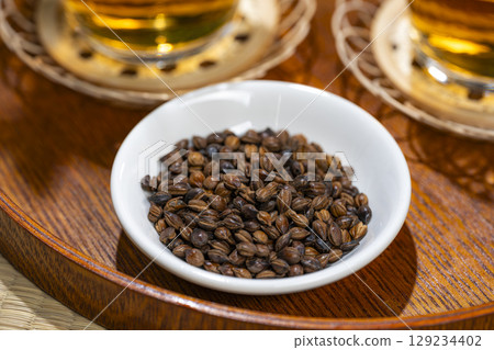 Whole barley grains in a white bowl with glasses of barley tea behind them Whole barley grains in a white bowl with glasses of barley tea behind them 129234402