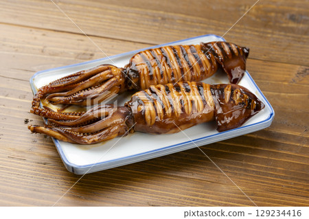 A Japanese-style dish of grilled squid with a fragrant brown finish, served on a plate 129234416