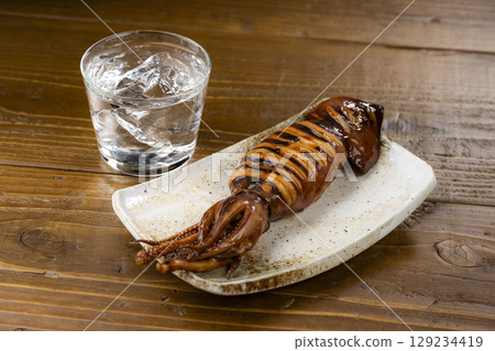 Grilled whole squid on a plate and a glass of cold shochu 129234419