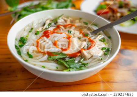 Pho soup with noodles and chicken meat, fresh greens, on a plate, Vietnamese cuisine, homemade food, on a table. Asian Noodle soup. Nobody, top view, close up 129234685