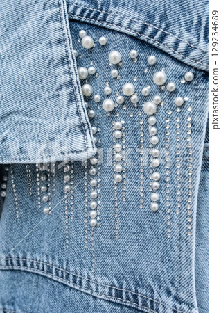 Denim jacket with fashionable embroidery of pearl beads. Blue denim fabric decorated with shiny silver beads decor. White pearls scattered on blue denim vest Denim jacket with fashionable embroidery of pearl beads. Blue denim fabric decorated with shiny silver beads decor. White pearls scattered on blue denim vest 129234689